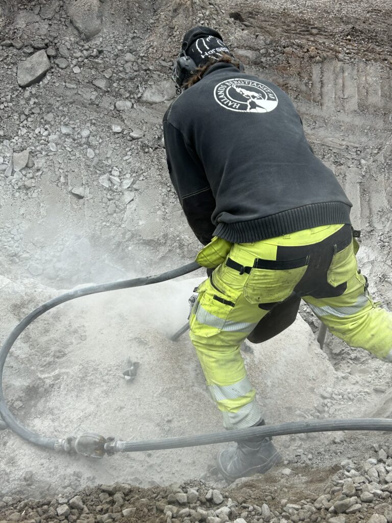 Hallandsbergtjänst tekniker spräcker berg med hydraulutrustning under aktivt markarbete